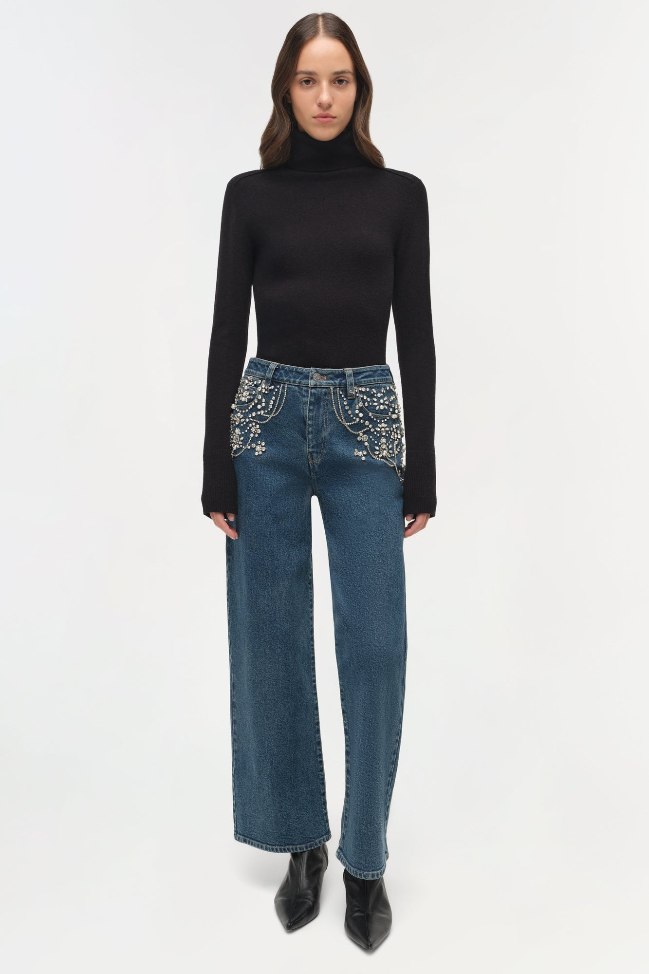 Blue denim crop jeans with silver rhinestone embellishments on pockets, styled with black turtleneck and boots.