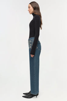 Woman wearing black crop turtleneck and blue jeans with crystal embellishments on back pockets, styled with black heeled boot