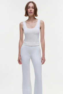 White sleeveless tank top with scoop neckline on model wearing matching white pants.