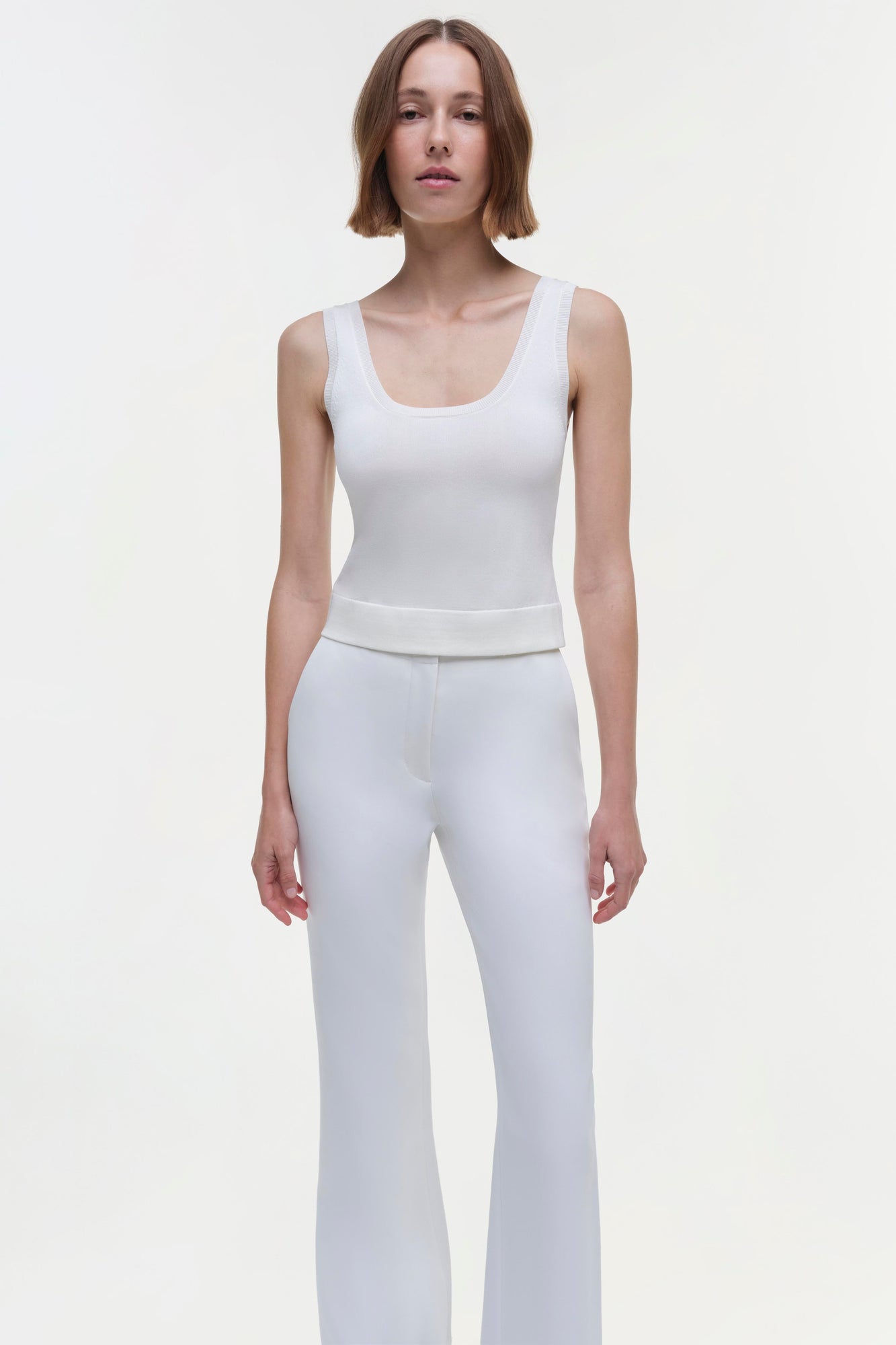 White sleeveless tank top with scoop neckline on model wearing matching white pants.