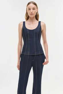 Woman wearing dark blue denim trousers with vertical topstitching and matching sleeveless denim top.