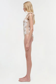 Woman wearing cream one-piece swimsuit with tan polka dot pattern, shown from the side.