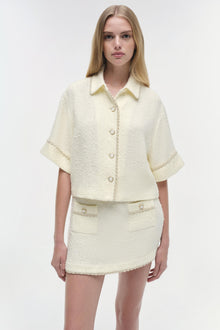 Cream textured mini skirt with front pockets and button details, shown on model with matching cropped jacket.
