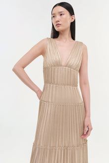 Beige pleated sleeveless gown with deep V-neckline and tiered horizontal seam details throughout.