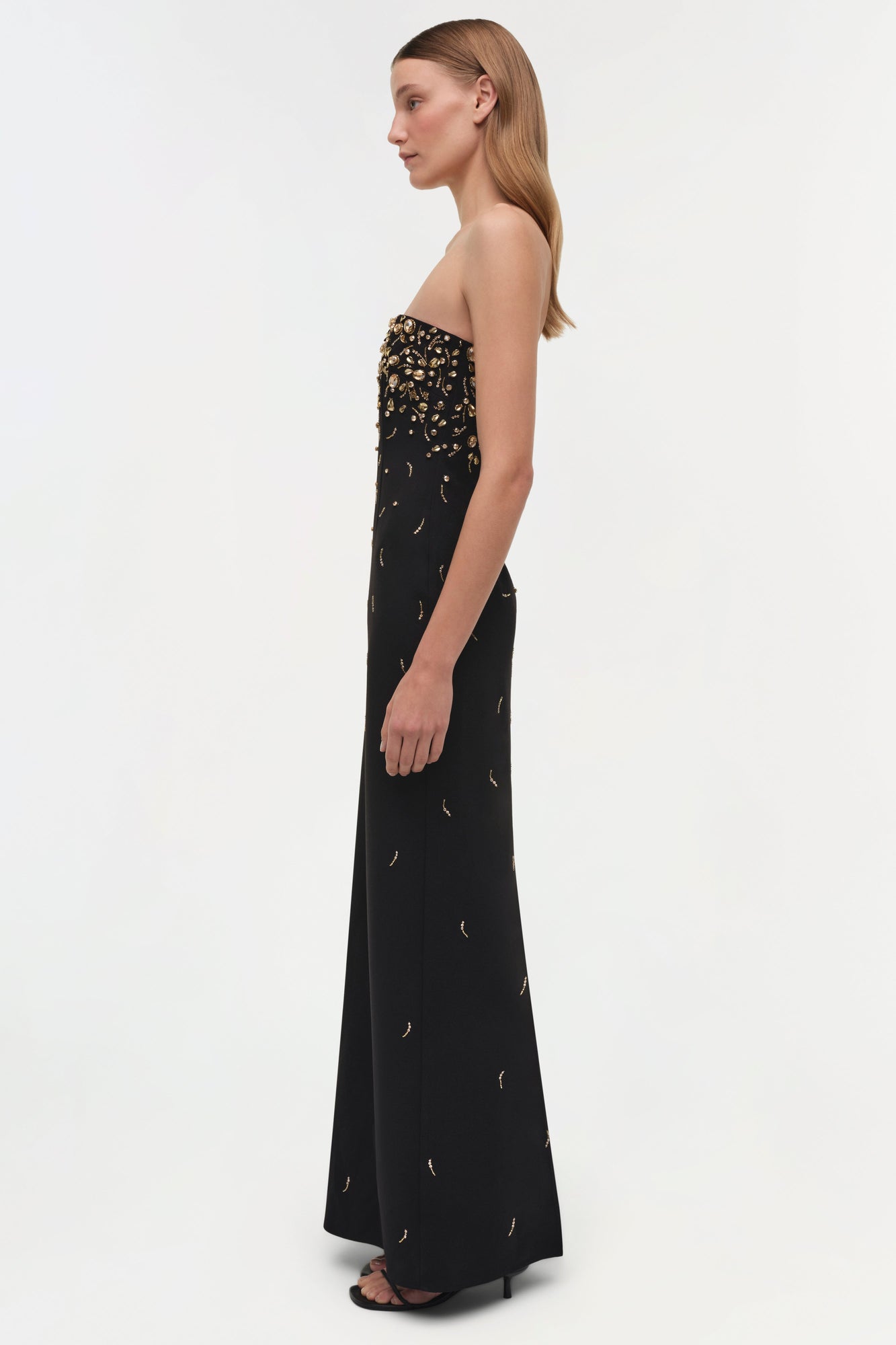 Black strapless gown with gold beaded embellishments concentrated at the bodice, worn with black heels.