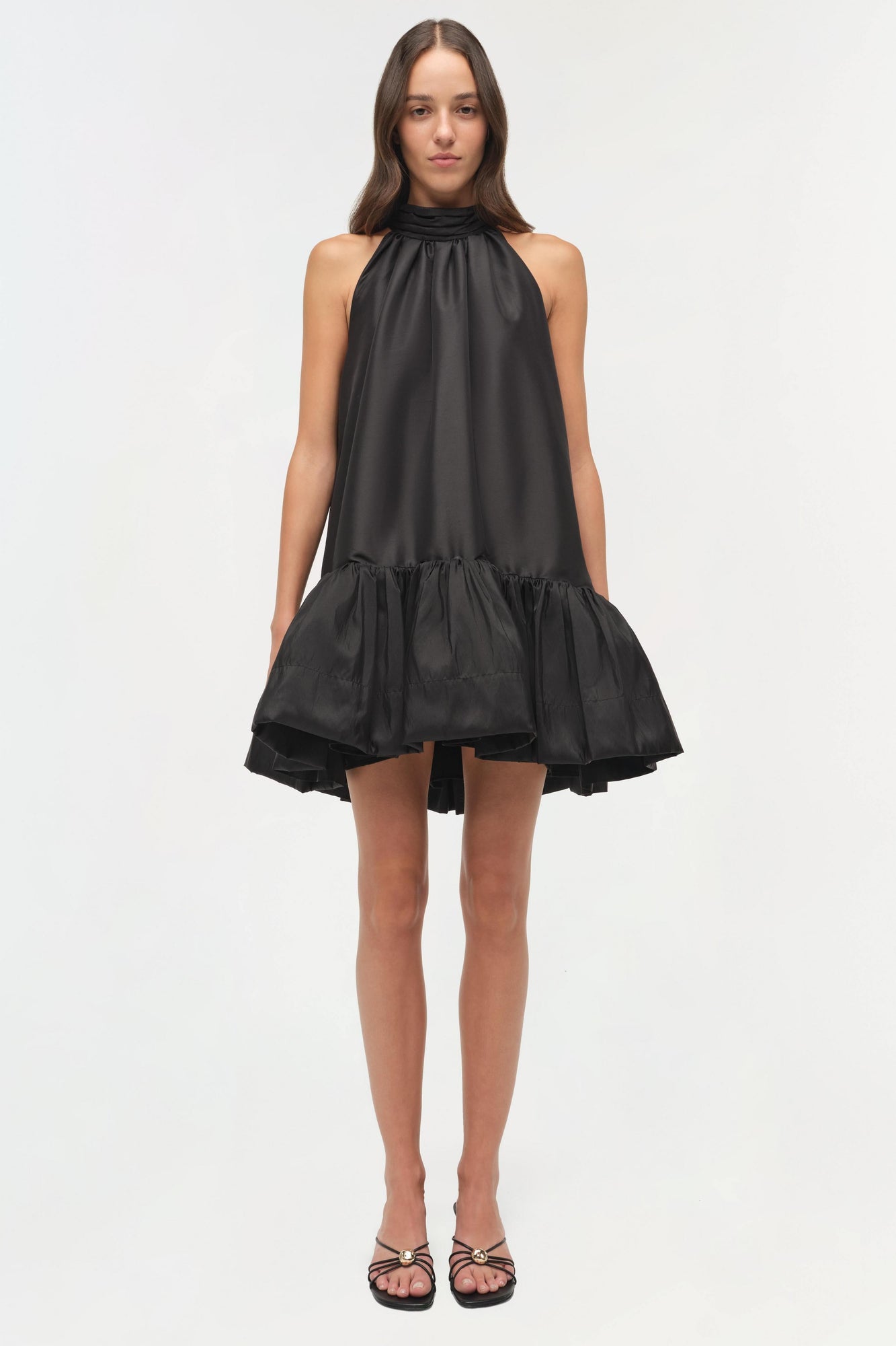 Black halter mini dress with gathered ruffle hem and bow neckline detail.