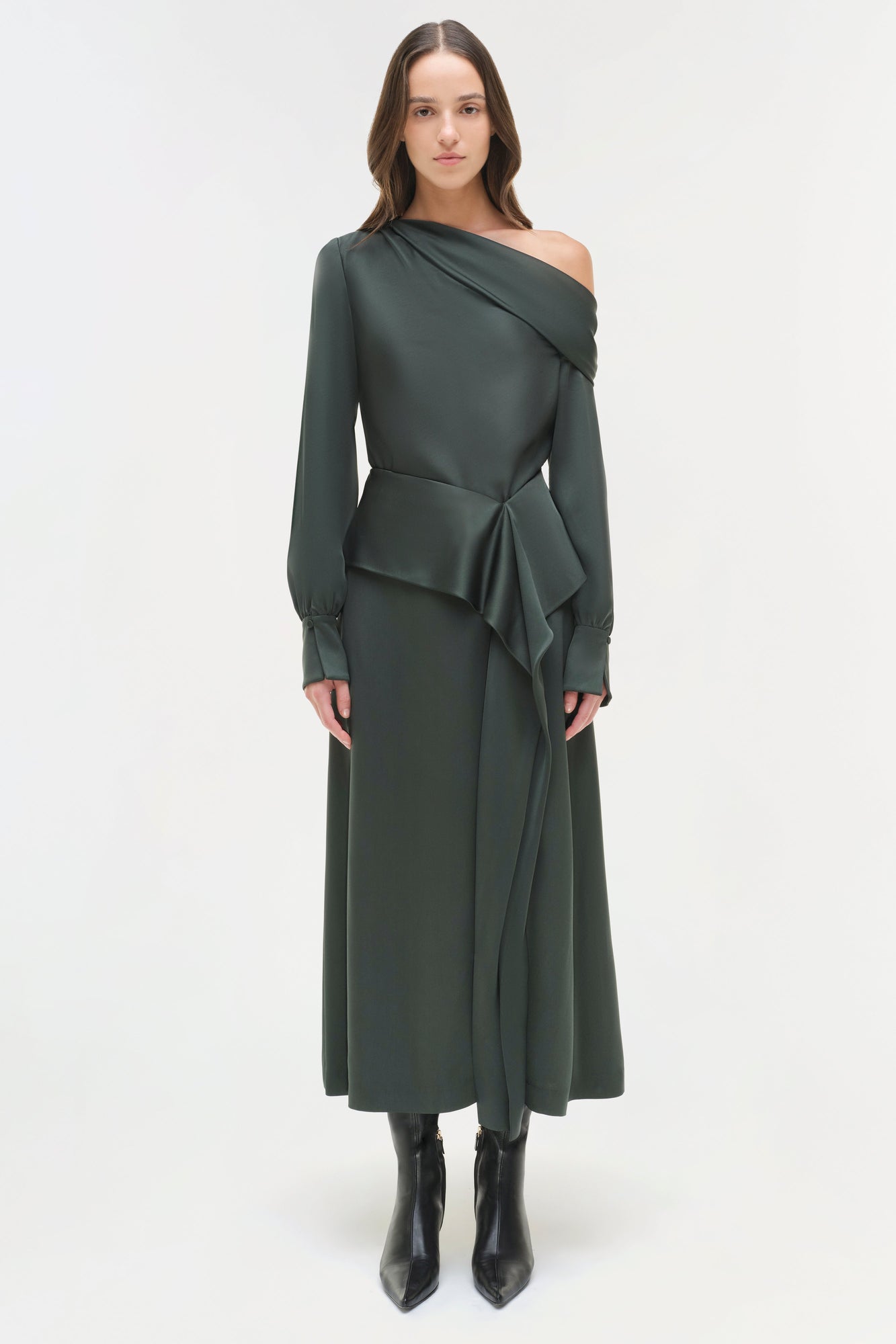 Woman wearing charcoal satin midi skirt with draped overlay and long sleeves, styled with black boots.