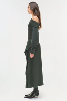 Woman wearing olive green satin midi skirt with off-shoulder long-sleeve top and black ankle boots, shown in profile view.