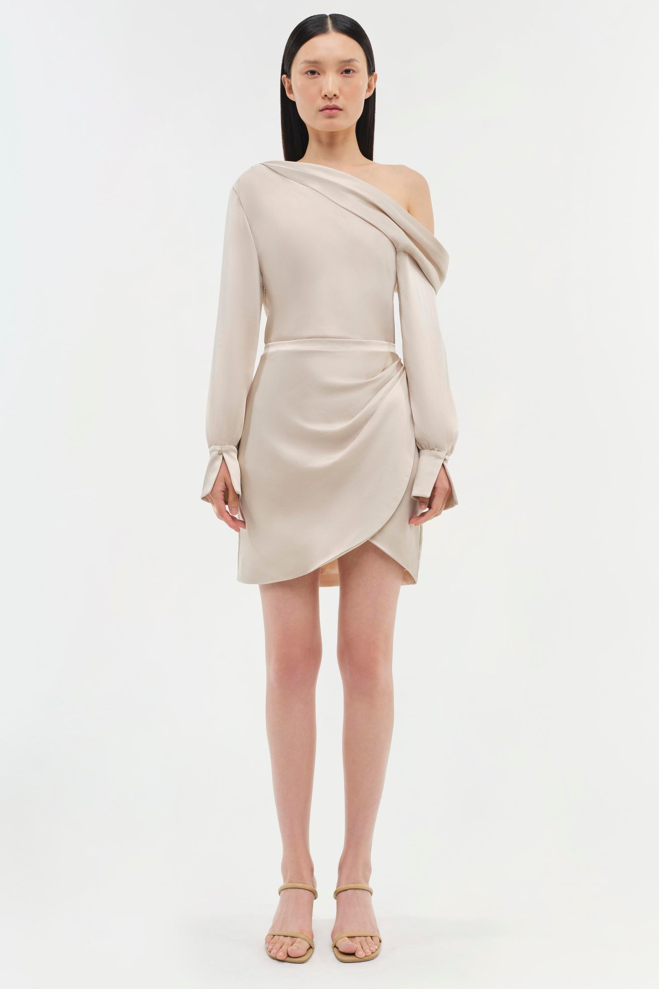 Beige off-shoulder dress with long sleeves, draped neckline, and asymmetrical wrap skirt detail.