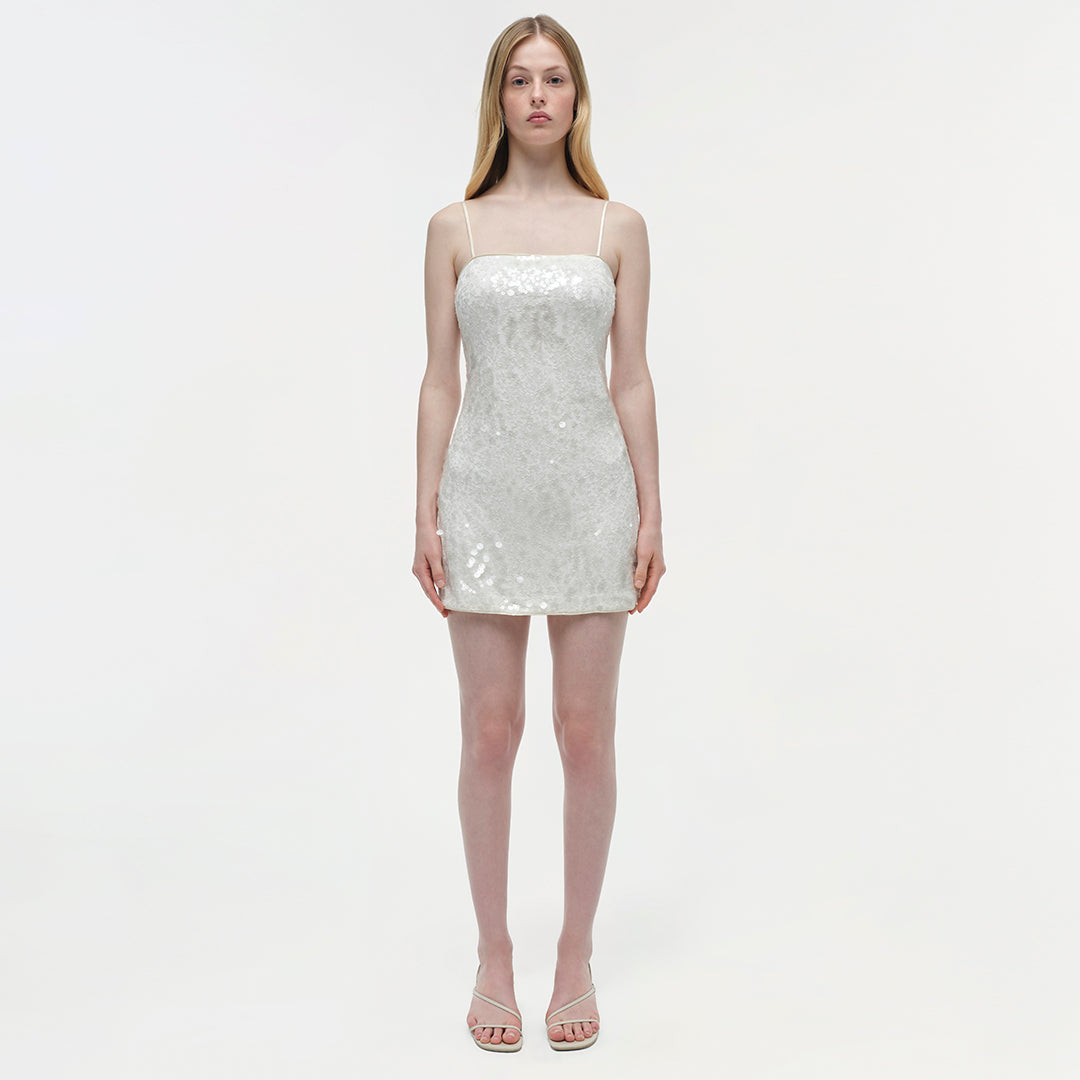 White sequined mini dress with thin straps on a model against a neutral background.