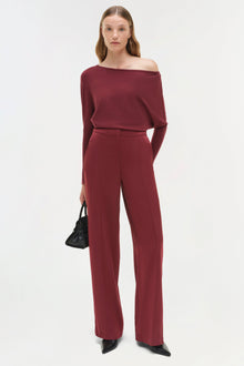 Woman wearing burgundy satin wide-leg pants with off-shoulder long-sleeve top and black pointed-toe shoes.