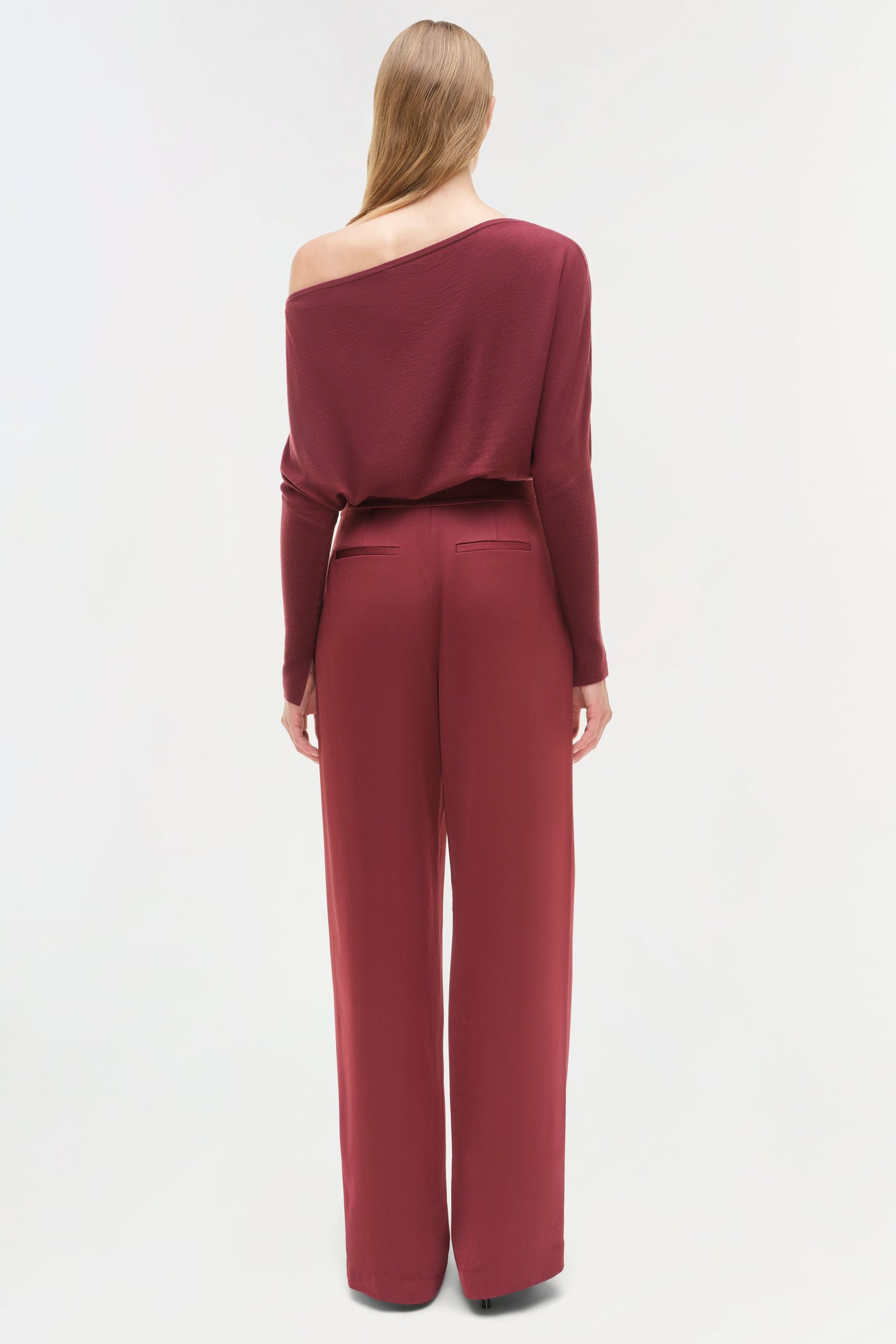 Woman wearing burgundy satin wide-leg pants with off-shoulder long-sleeve top, shown from back view.
