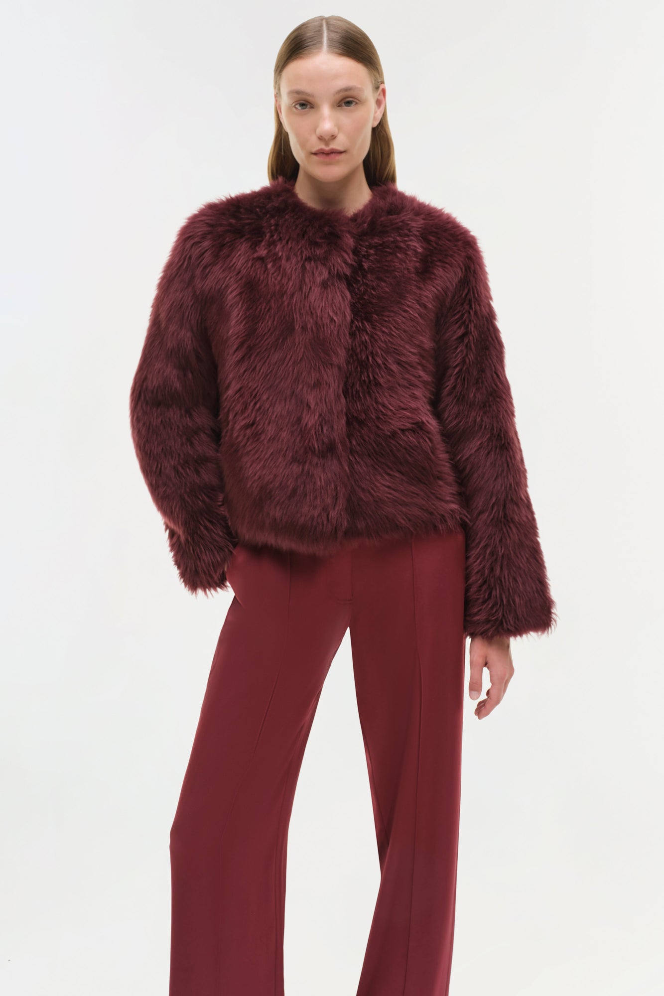 Burgundy shearling jacket with fuzzy texture and crew neckline, styled with matching trousers.