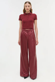 Burgundy leather wide-leg pants with high waist and pleated front, paired with matching polo shirt.