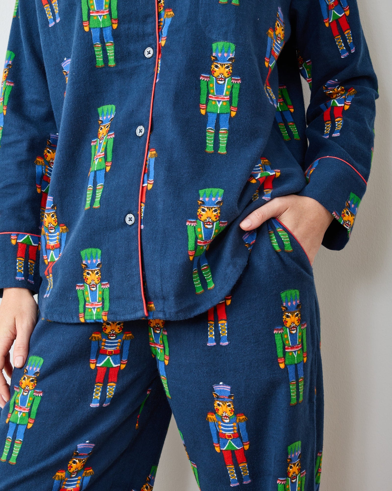 Close-up of navy pajama set with colorful leopard nutcracker print, red piping, buttons, and pants pocket