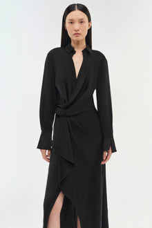 Black wrap dress with collared neckline, long sleeves with cuffed hems, and asymmetrical draped skirt with side slit.