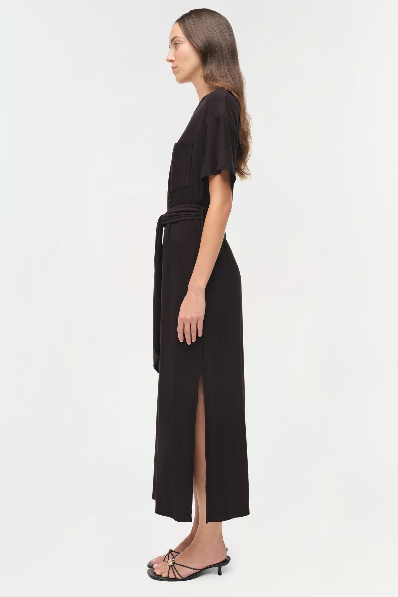 Black jersey t-shirt dress with short sleeves, drawstring waist, and front slit, shown on model in profile view.