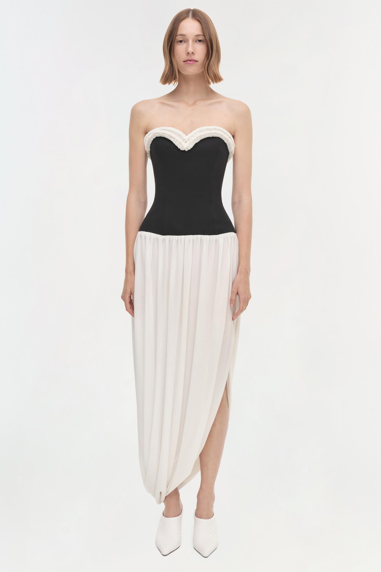 Strapless dress with black fitted bodice, white beaded neckline trim, and cream pleated asymmetrical skirt.