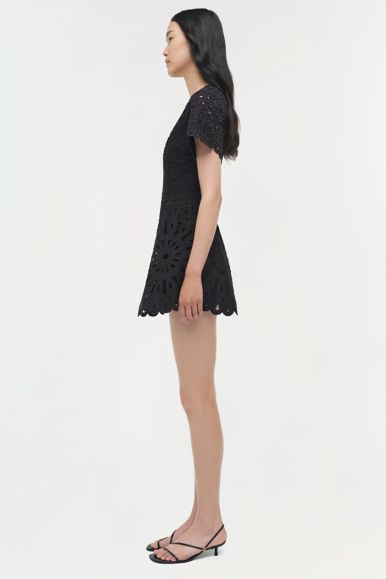 Black embroidered mini dress with short sleeves and scalloped hem, worn with black strappy heels.