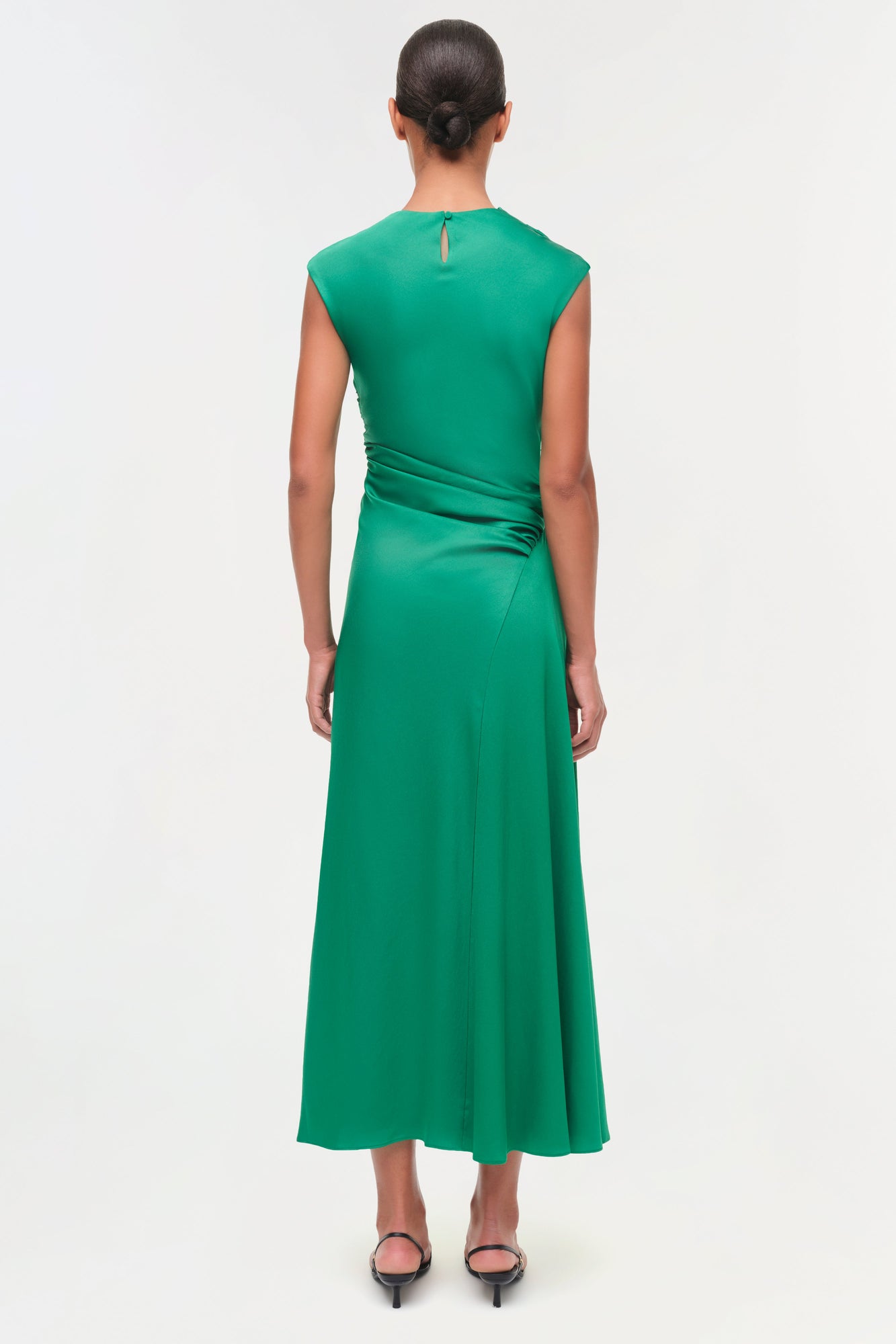 Woman wearing a sleeveless emerald green satin midi dress with ruched draping at the waist, shown from back view.
