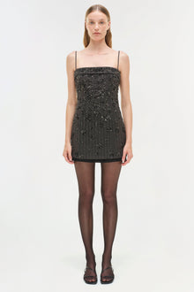 Black mini dress with beaded embellishments, thin straps, and straight neckline on model wearing tights.