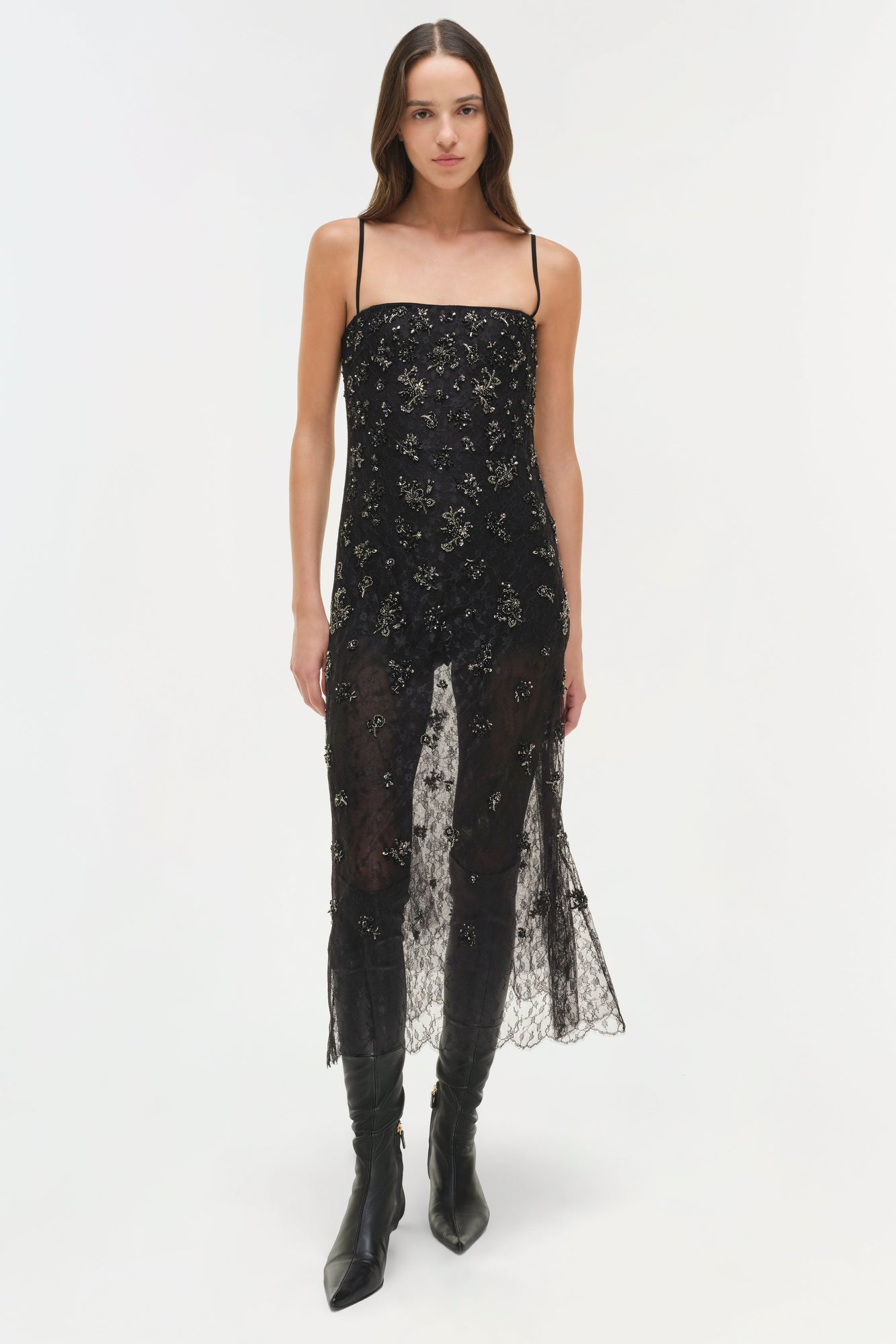 Black lace midi dress with embellishments and asymmetrical hem worn with black boots.