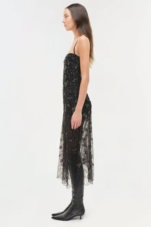 Black lace midi dress with beaded embellishments and asymmetrical hemline, worn with black knee-high boots.