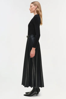 Woman wearing black knit midi dress with leather pleated skirt and belt, shown in profile view.