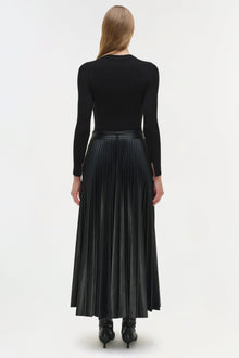 Woman wearing black knit midi dress with long sleeves and pleated faux-leather skirt, shown from back.