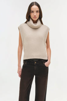 Cream ribbed sleeveless turtleneck top with cropped fit worn with black denim pants.