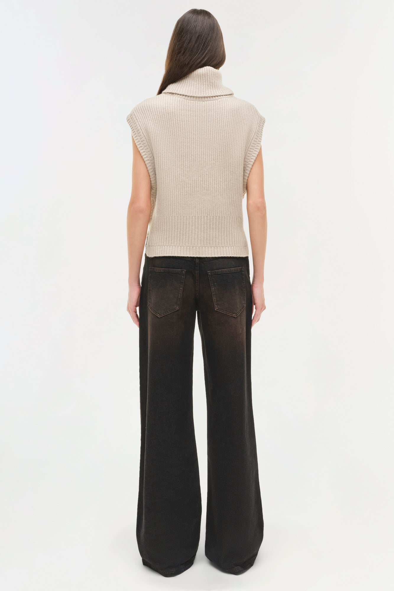 Woman wearing beige sleeveless ribbed turtleneck and black wide-leg denim jeans, shown from back.