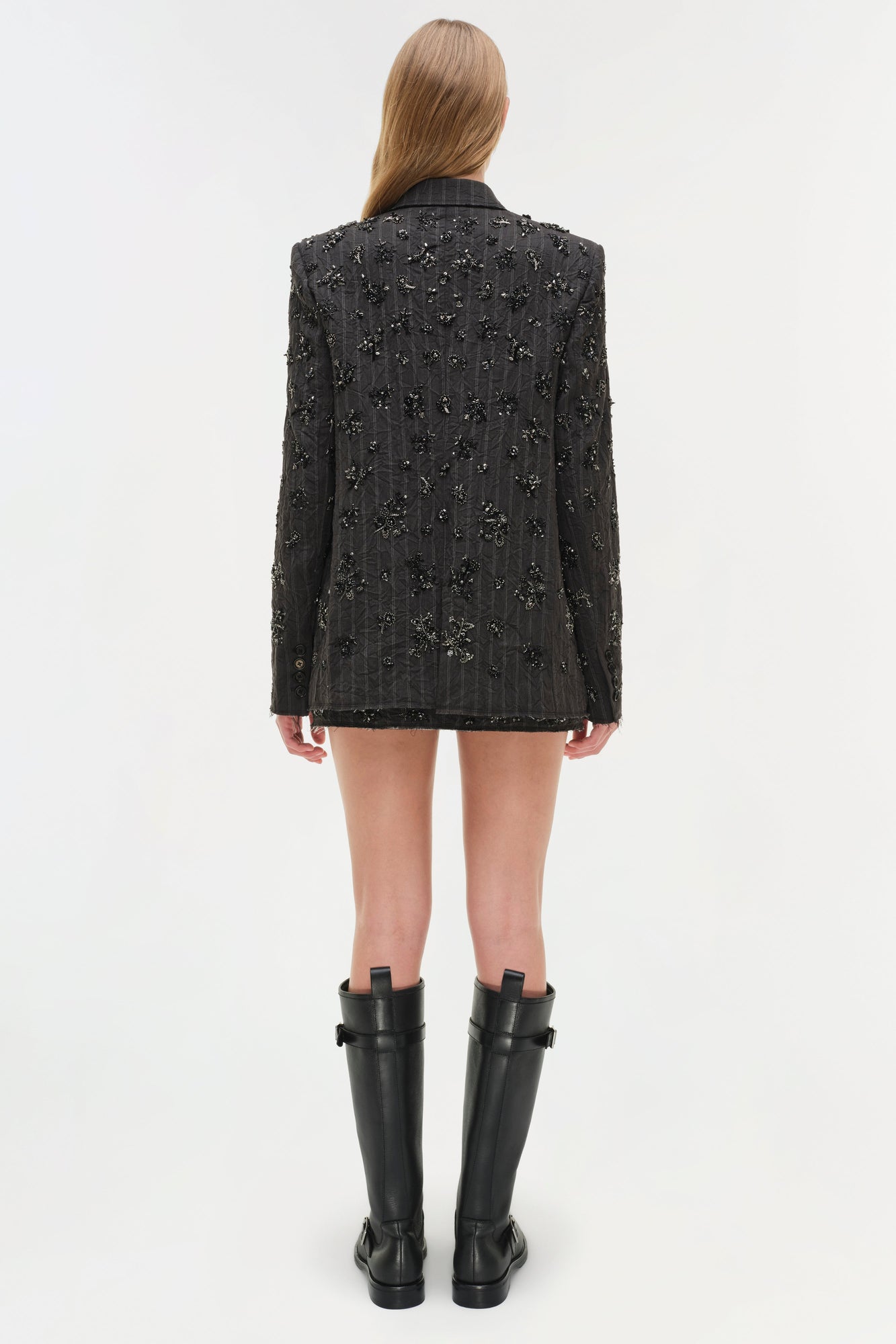 Black pinstriped blazer with scattered crystal embellishments throughout, worn with black knee-high boots.