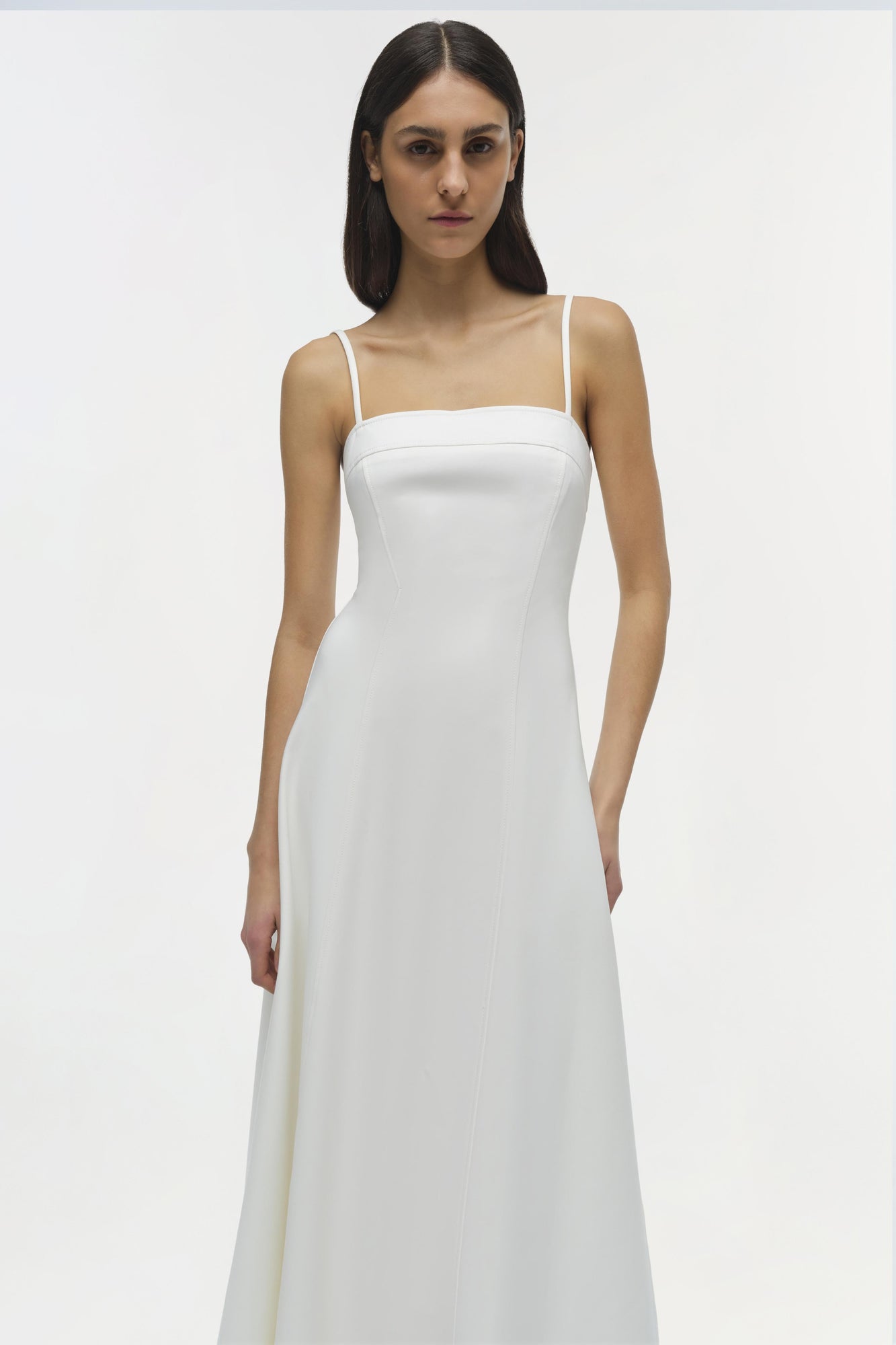 Woman wearing white sleeveless midi dress with square neckline and thin straps.