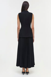 Woman wearing black sleeveless dress with fitted bodice and pleated midi skirt, shown from back view.