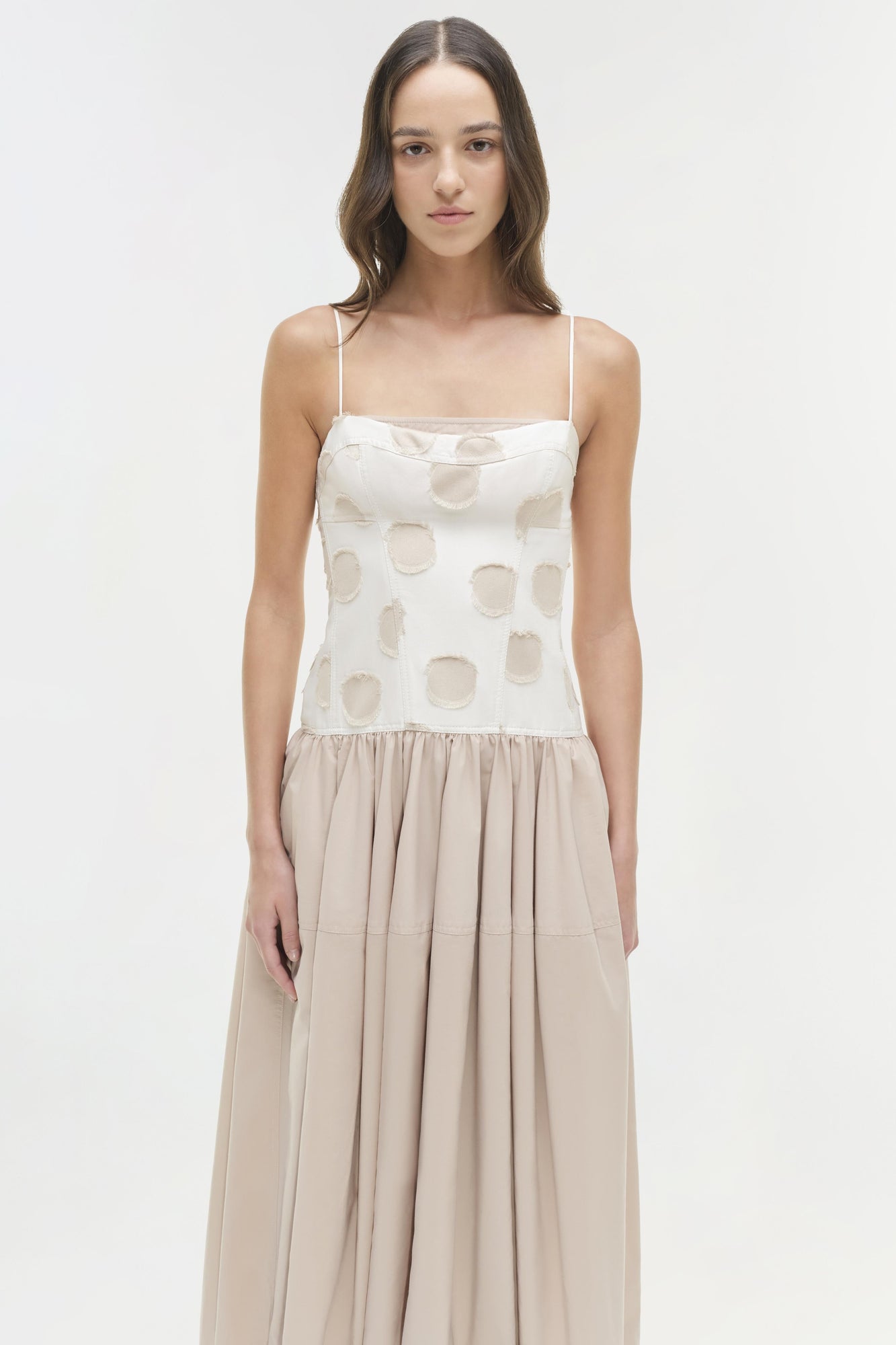 Woman wearing white midi dress with circular cutout pattern on bodice and beige gathered skirt.