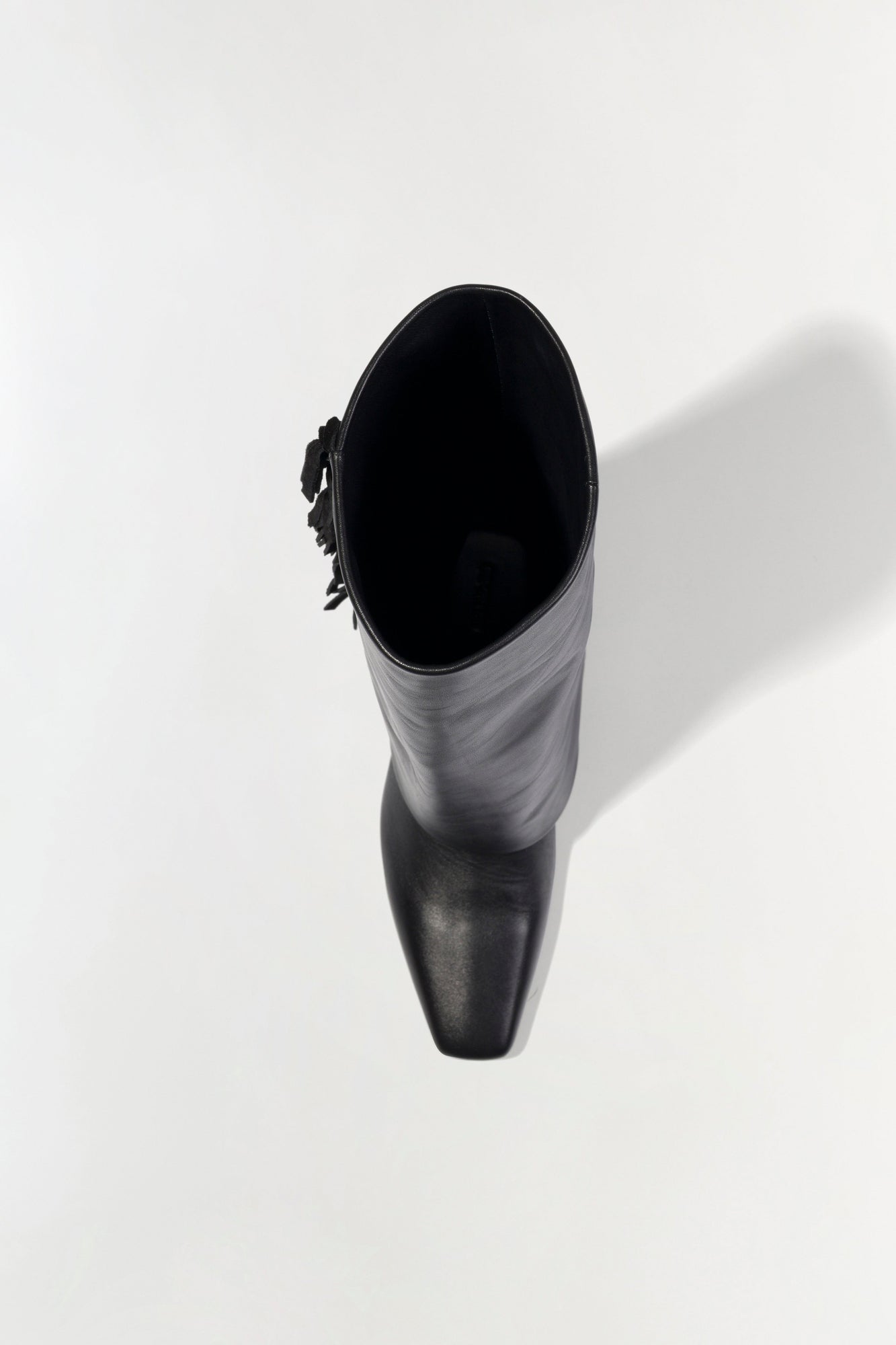 Black leather boot with fringe detail on the cuff, shown from above with lace-up closure at the top.