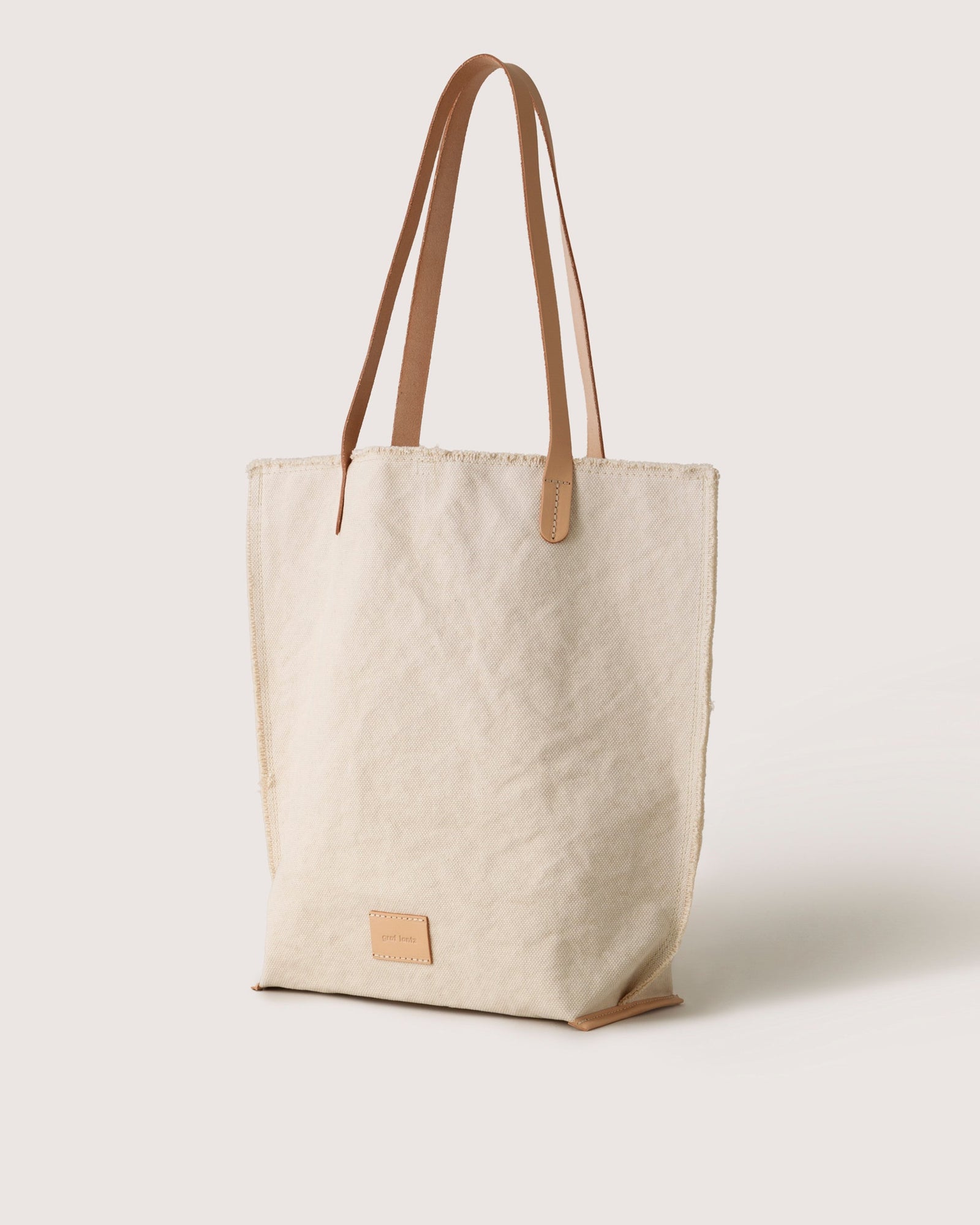 The graf lantz Hana Canvas Tote combines durable cotton canvas with brown leather handles and a small leather patch at the base, all set against an eye-catching beige exterior.