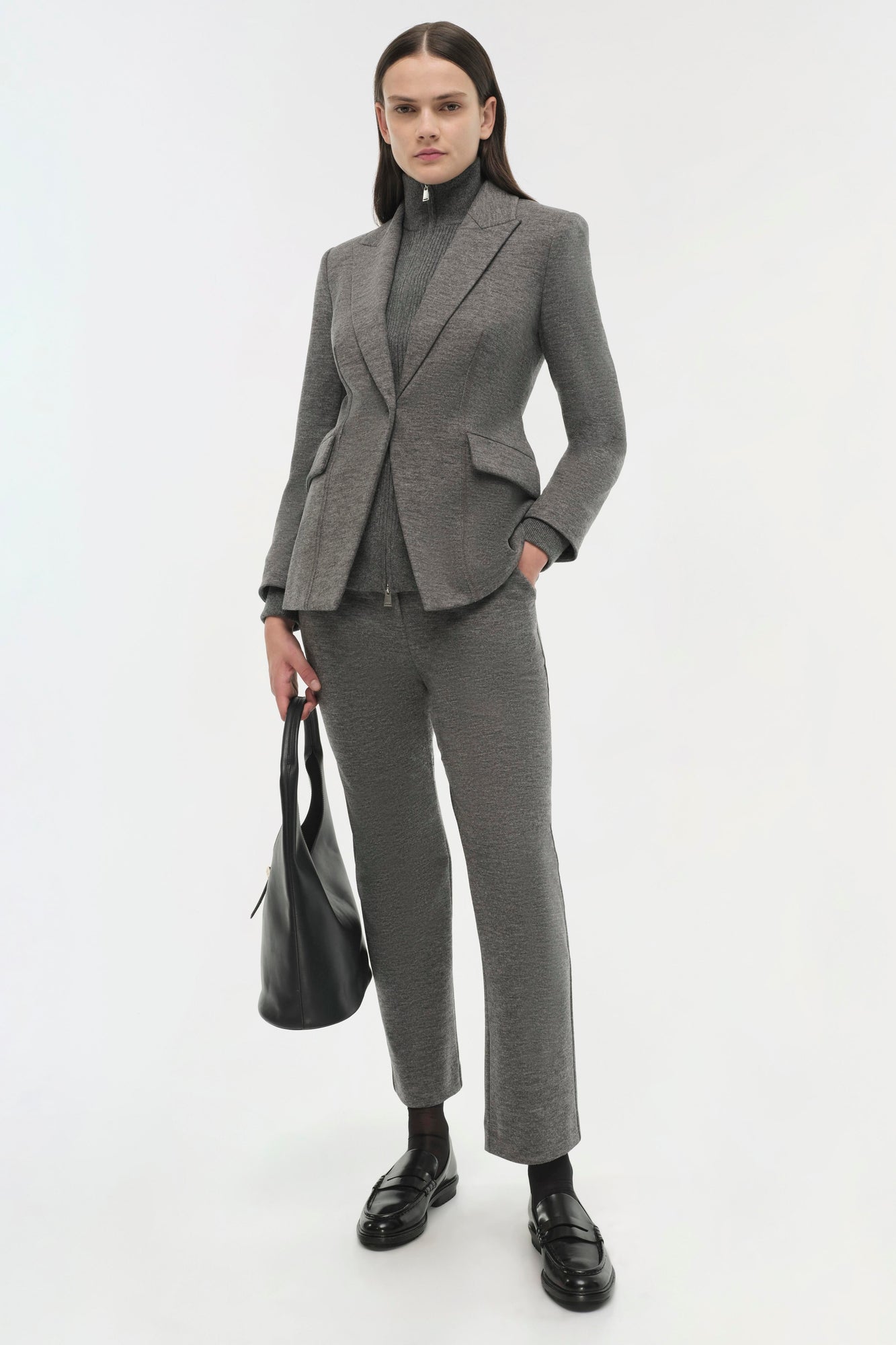 Woman wearing gray wool Auden Blazer with matching pants, black loafers, and holding a black leather tote bag.