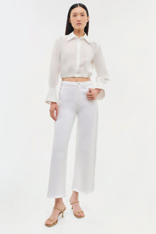 White button-up crop top with long sleeves and collar, paired with white wide-leg jeans.
