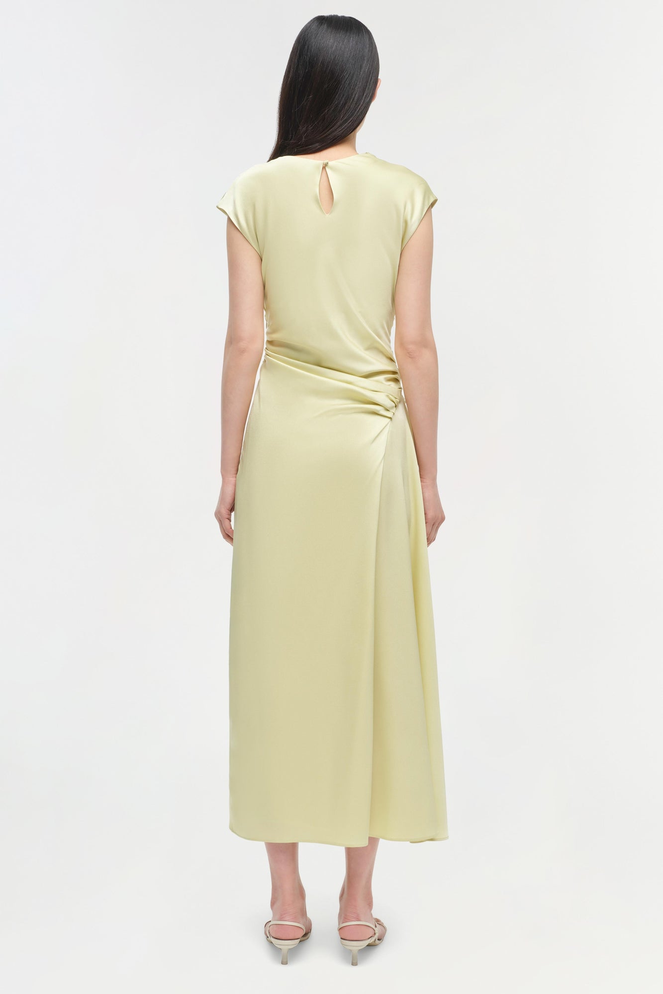 Pale yellow satin midi dress with short capped sleeves, keyhole back detail, and ruched side waist on model.