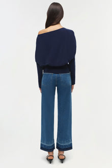 Navy blue off-shoulder cropped sweater with long sleeves worn with blue jeans.