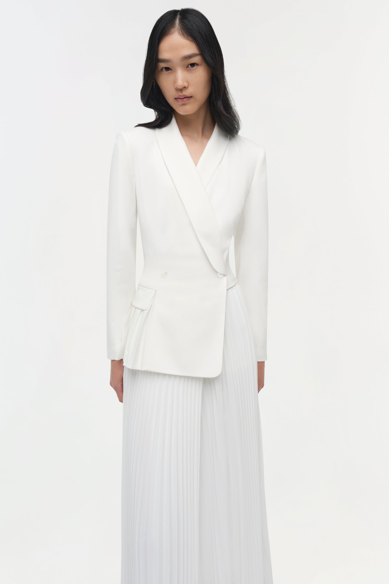 Woman wearing a cream blazer dress with pleated skirt detail and long sleeves.