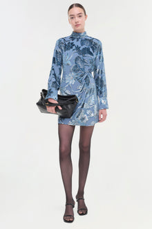 Woman wearing blue floral velvet dress with high neckline and long sleeves, styled with black tights and sandals.