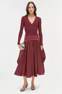 Woman wearing burgundy ribbed knit cardigan and full taffeta midi skirt with black strappy sandals.