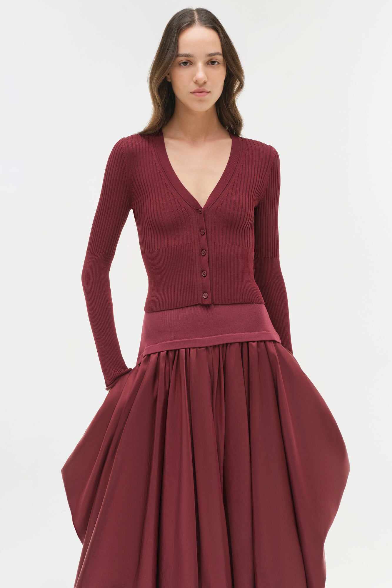 Woman wearing burgundy ribbed knit cardigan with button front paired with midi skirt with gathered taffeta skirt portion.