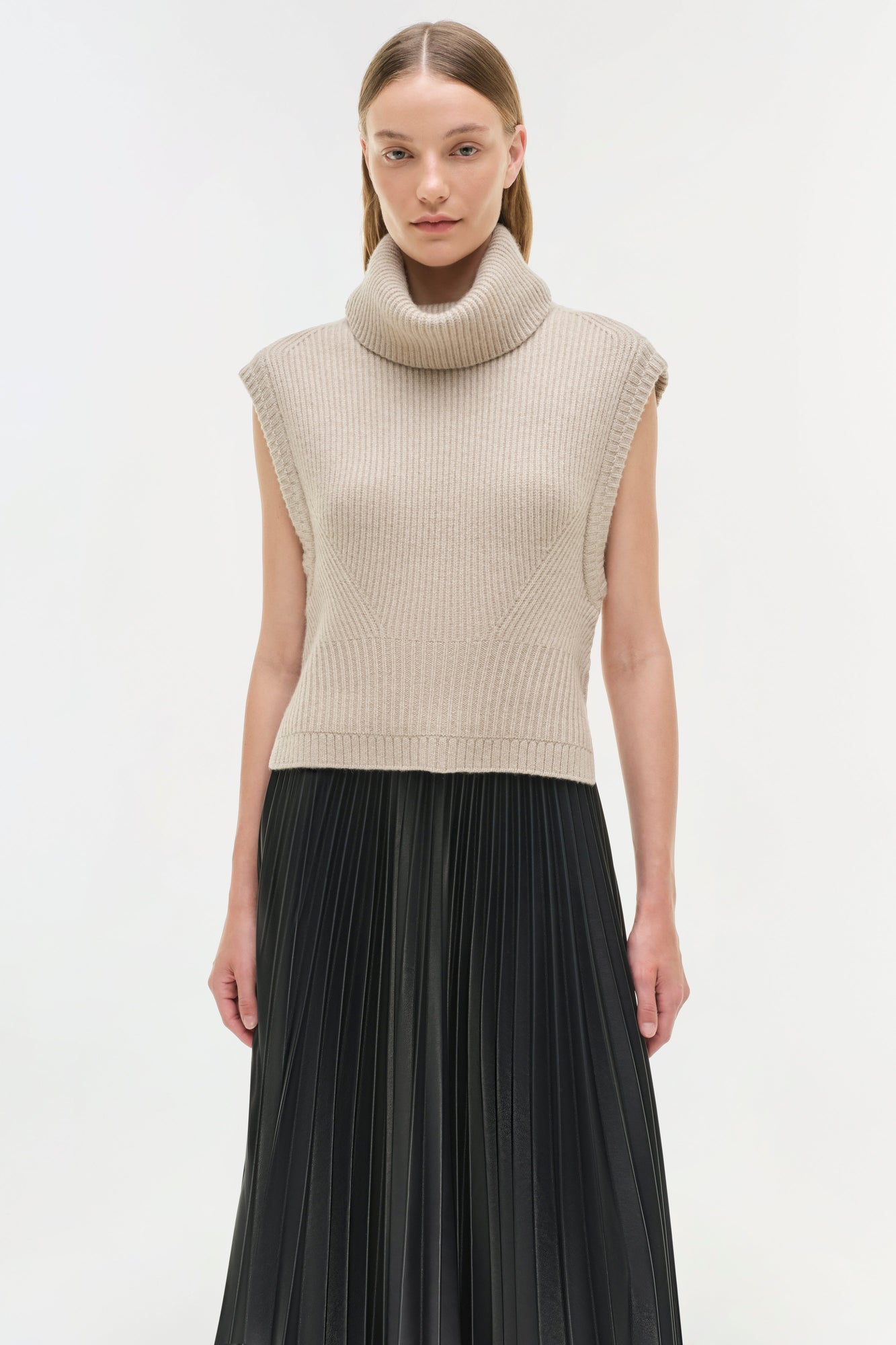 Black pleated midi skirt worn with a beige ribbed turtleneck sleeveless sweater.