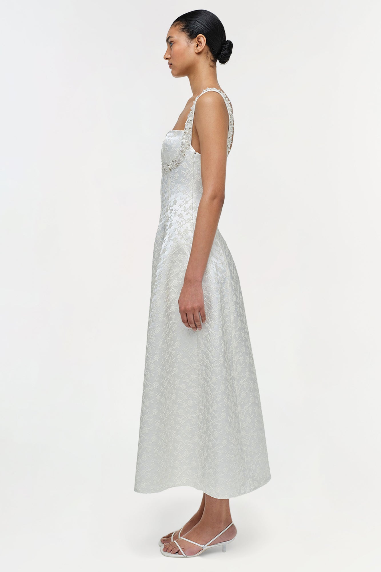 Woman wearing a sleeveless light gray jacquard midi dress with a fitted bodice and A-line skirt, shown from the side.