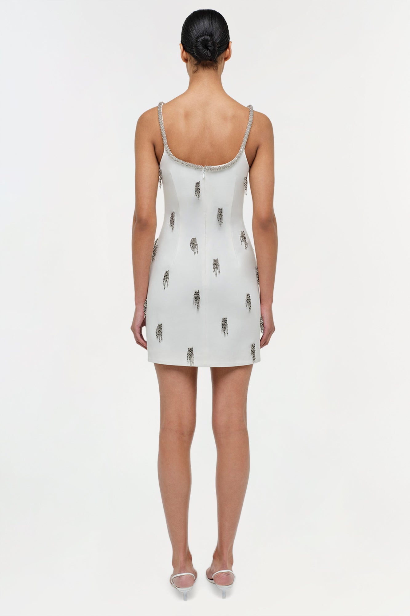 White mini dress with silver beaded neckline and scattered tassel embellishments throughout, shown on model from back.