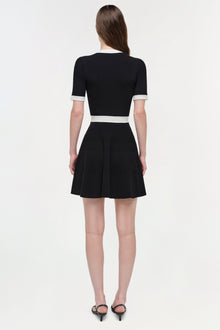 Black ribbed knit mini dress with white trim at neckline, cuffs, and waistband, shown on model from back.