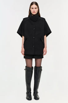 Black wool cape jacket with button front, high neckline, and short sleeves worn with black boots.